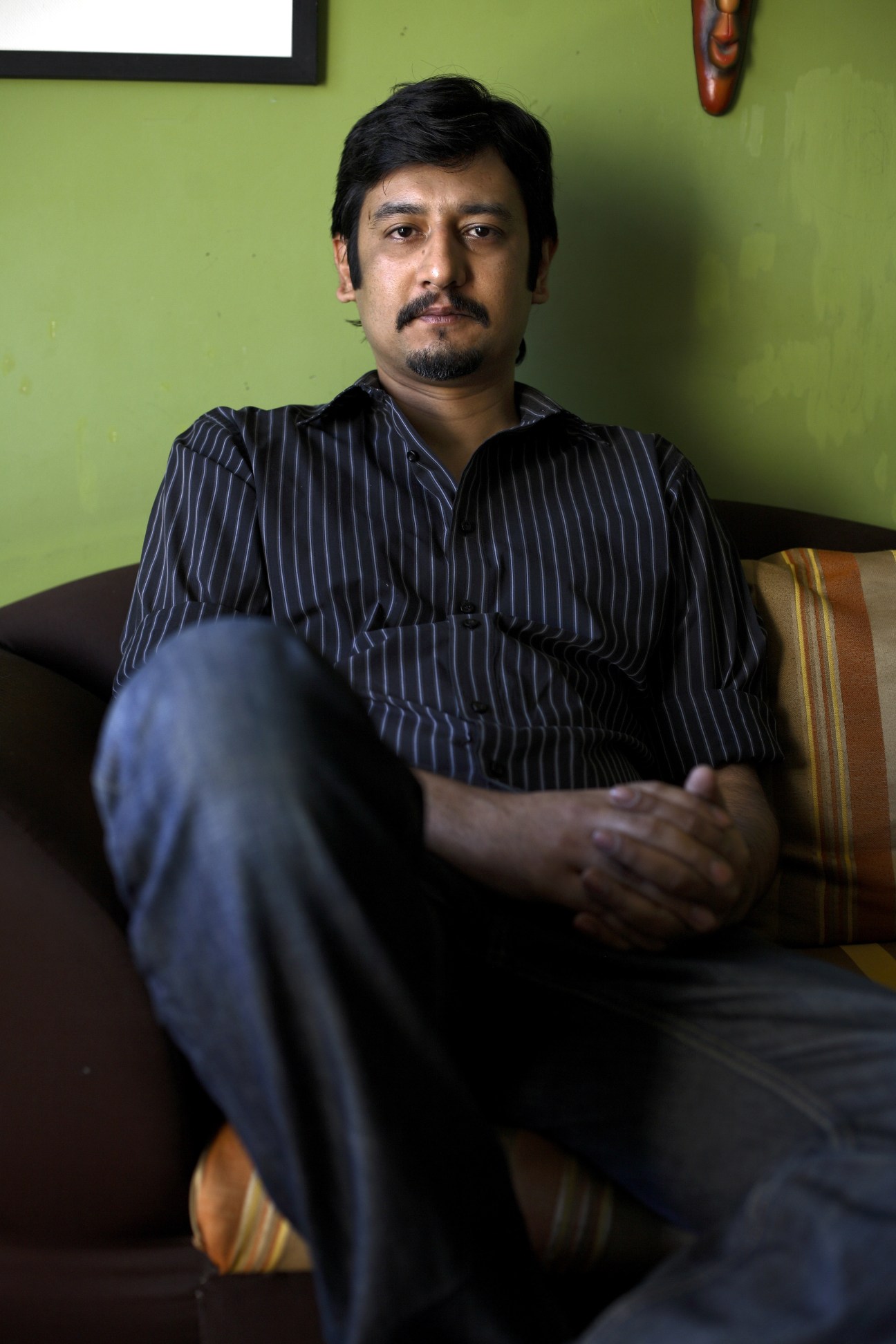 Umar Amanullah, senior producer for GEO TV, seated against a lime green wall wearing a dark pinstriped shirt.