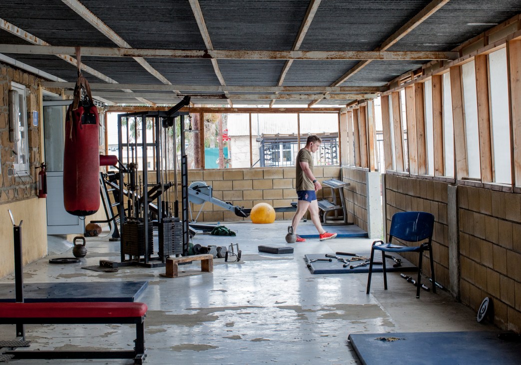 A soldier exercises in a sparse gym facility with punching bag, kettlebells and weights at Blue Beret Camp.