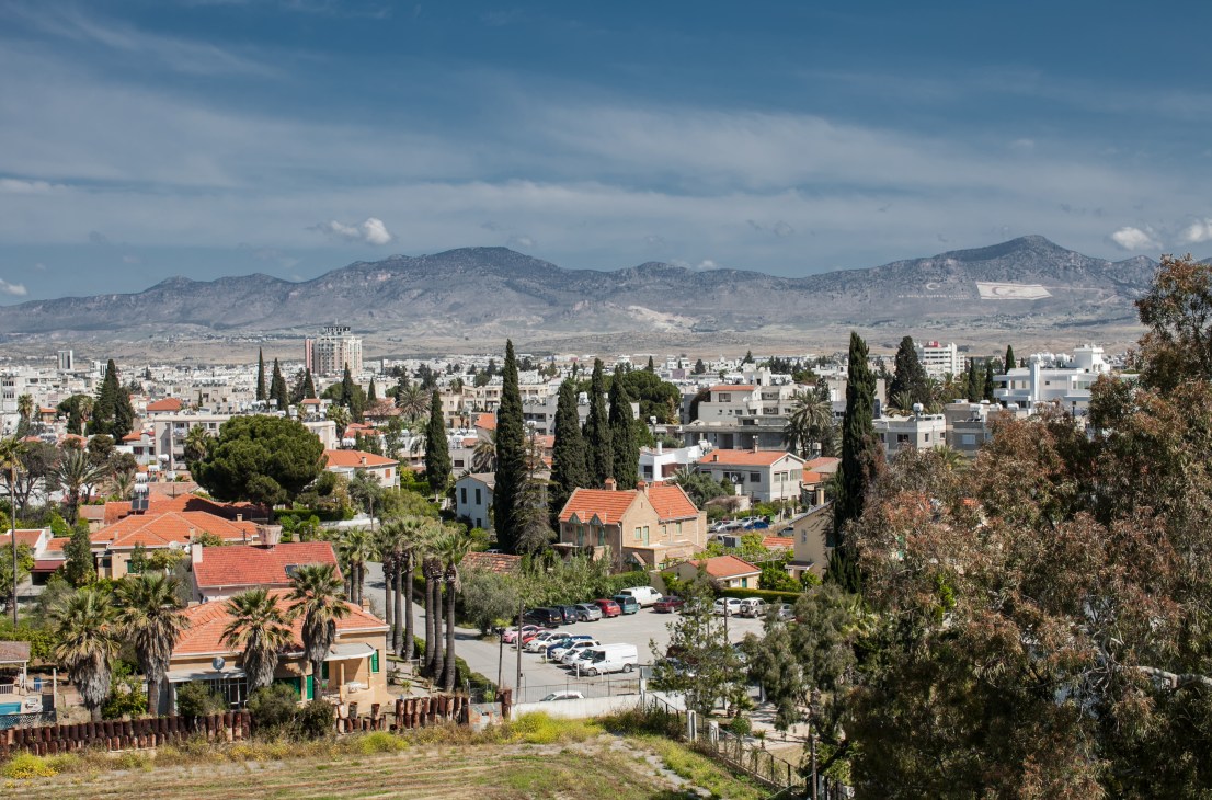 Aerial view of divided Nicosia showing Greek and Turkish sides with mountains and painted flag in background.