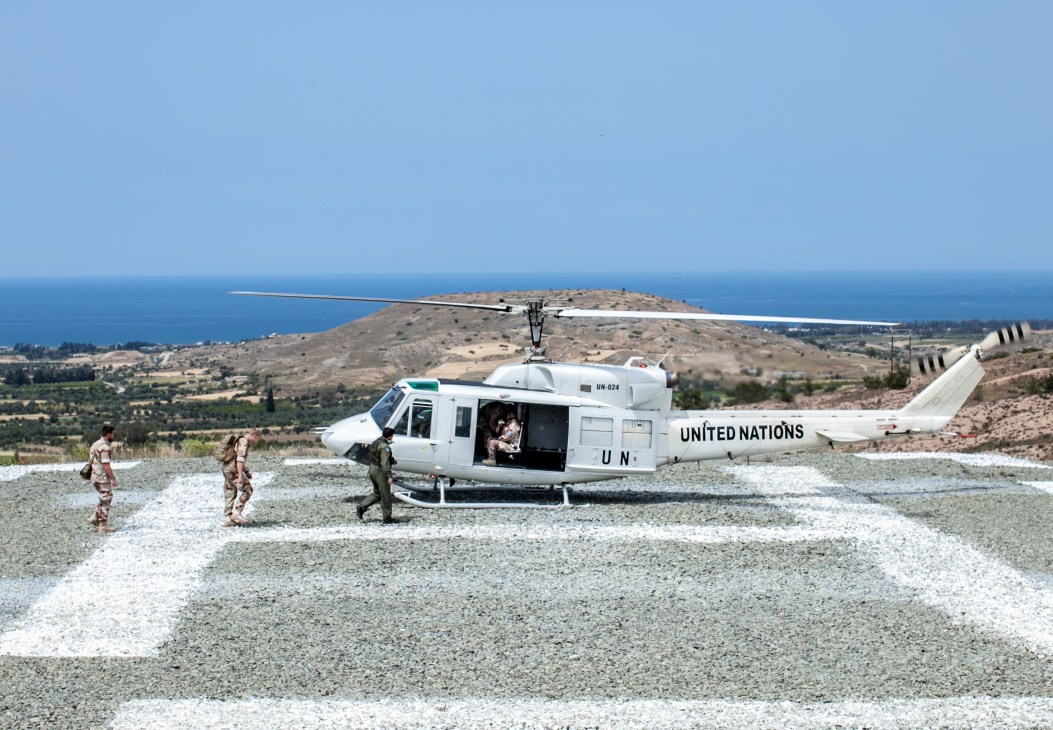Major General Kristin Lund boarding a UN helicopter on a gravel landing pad overlooking Cyprus coastline and mountains.