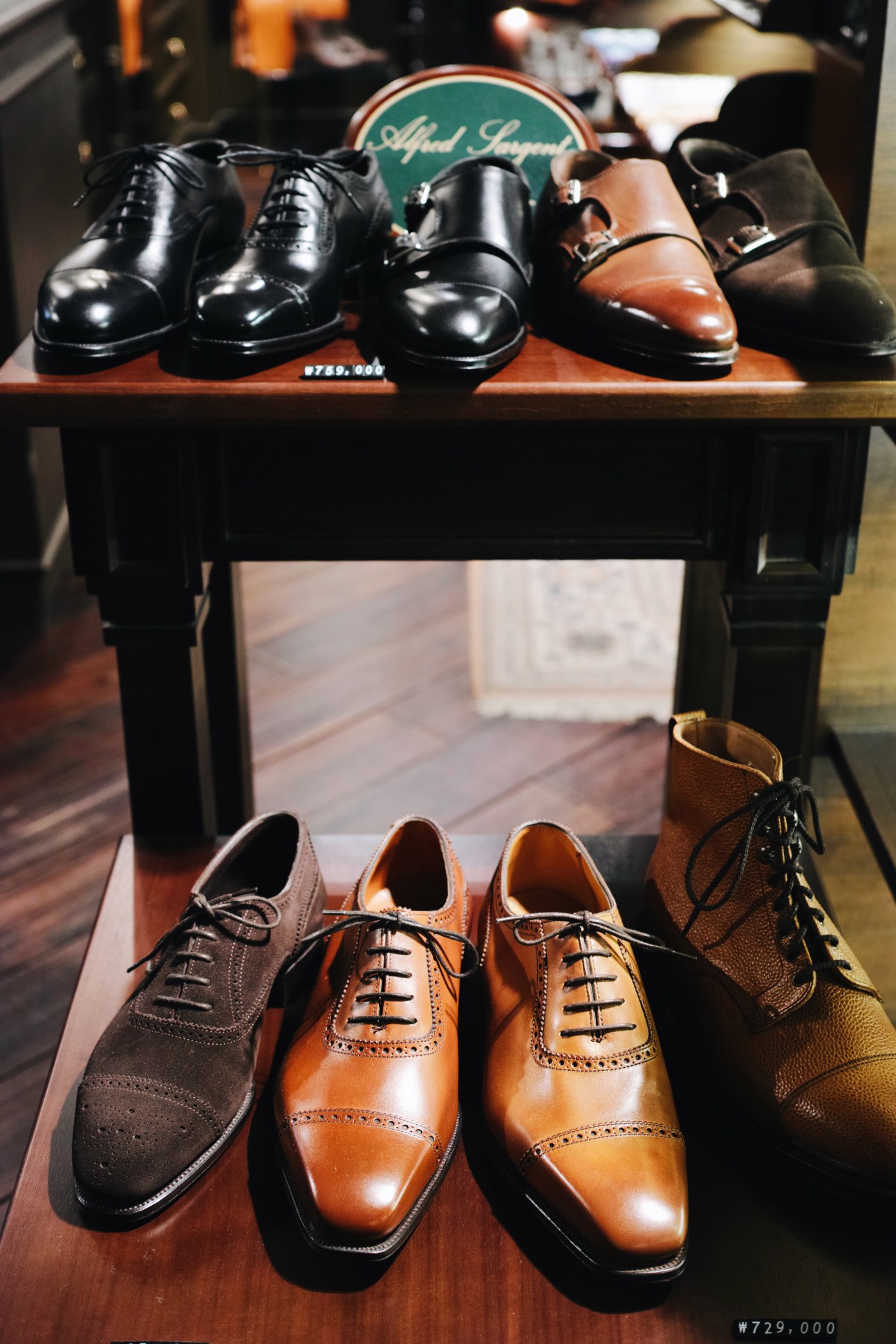 Alfred Sargent shoes displayed on two wooden shelves, including black oxfords, cognac brogues, and brown leather styles.