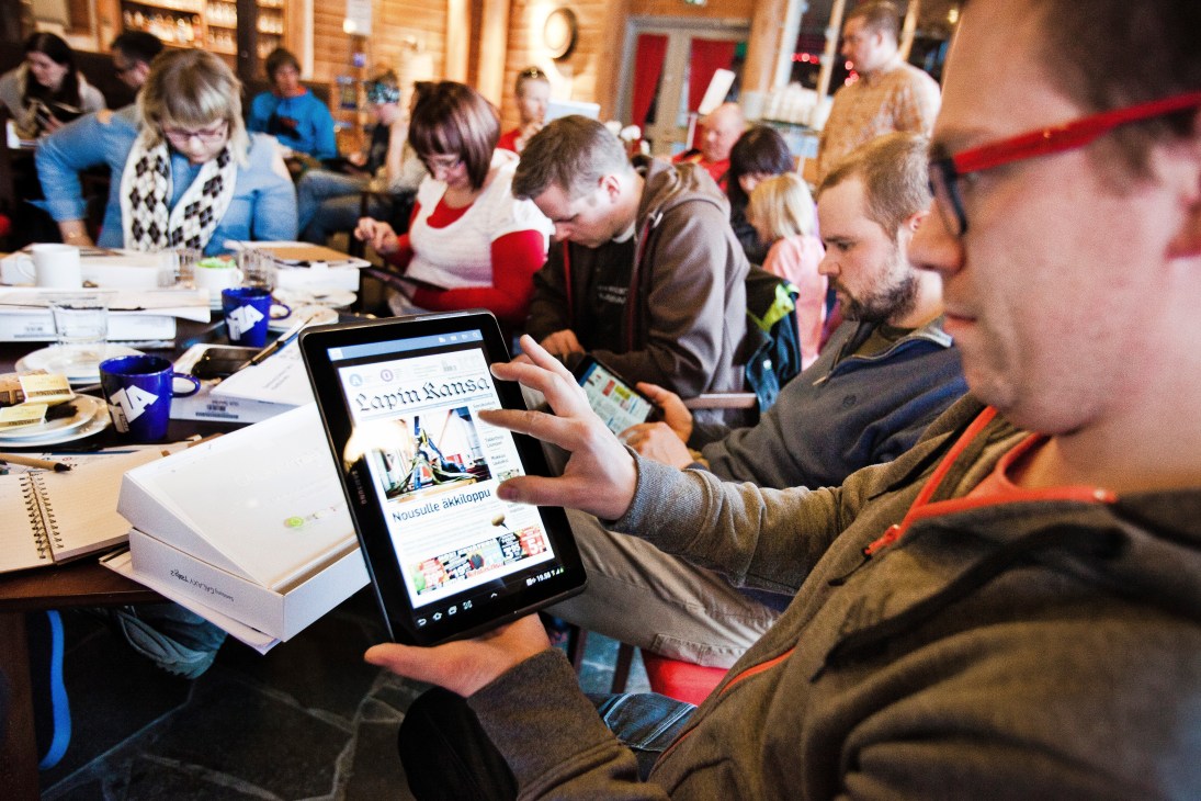 Group of people at a table viewing Lapin Kansa newspaper on a tablet device.