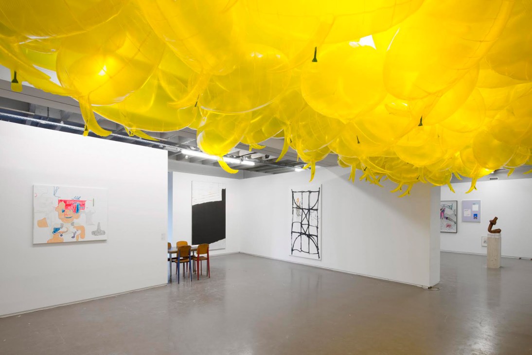 Art gallery space with yellow fabric installation overhead and contemporary artworks on white walls