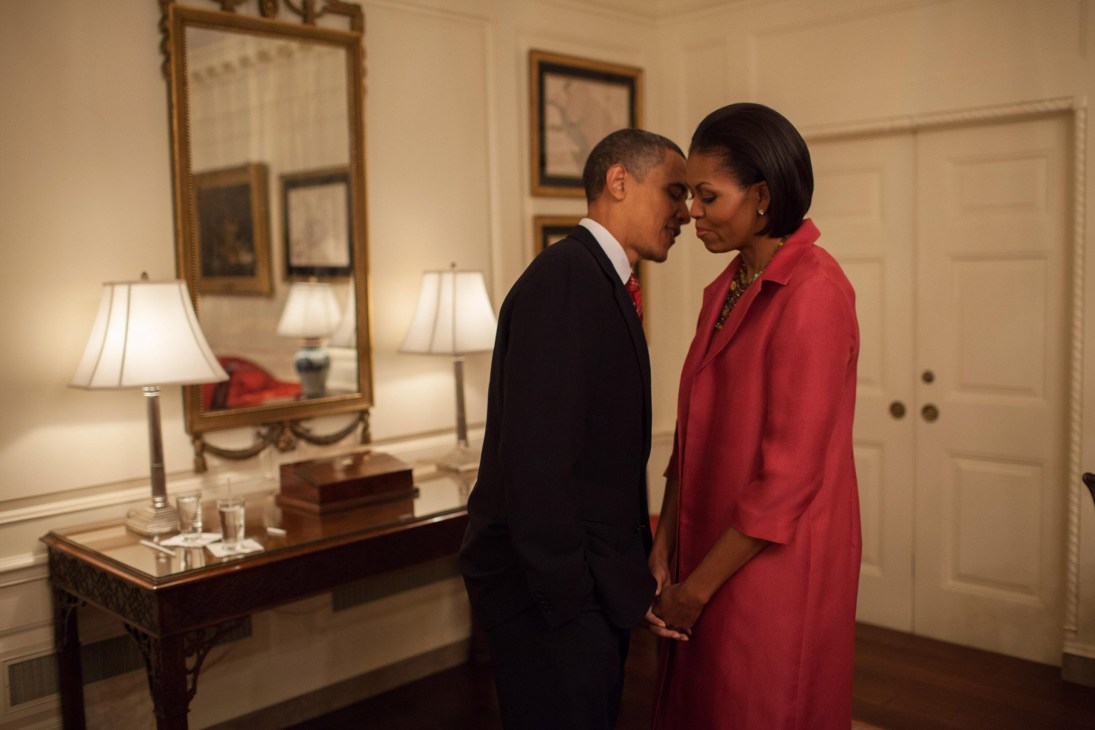 Barack Obama and Michelle Obama stand close together in an elegant White House room with formal furnishings and mirrors.