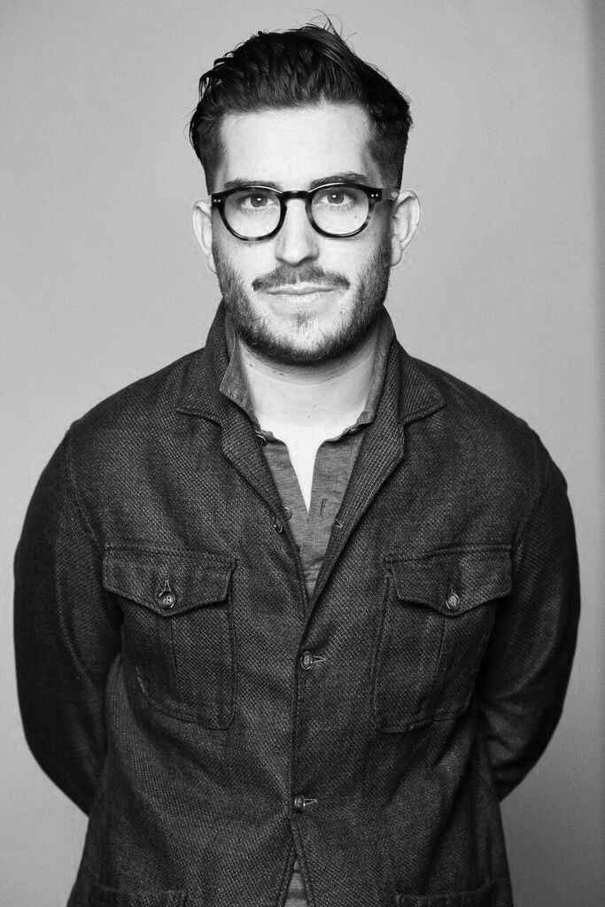 Christian Kimber, a man wearing black-framed glasses and a dark textured shirt, in a black and white portrait photograph.
