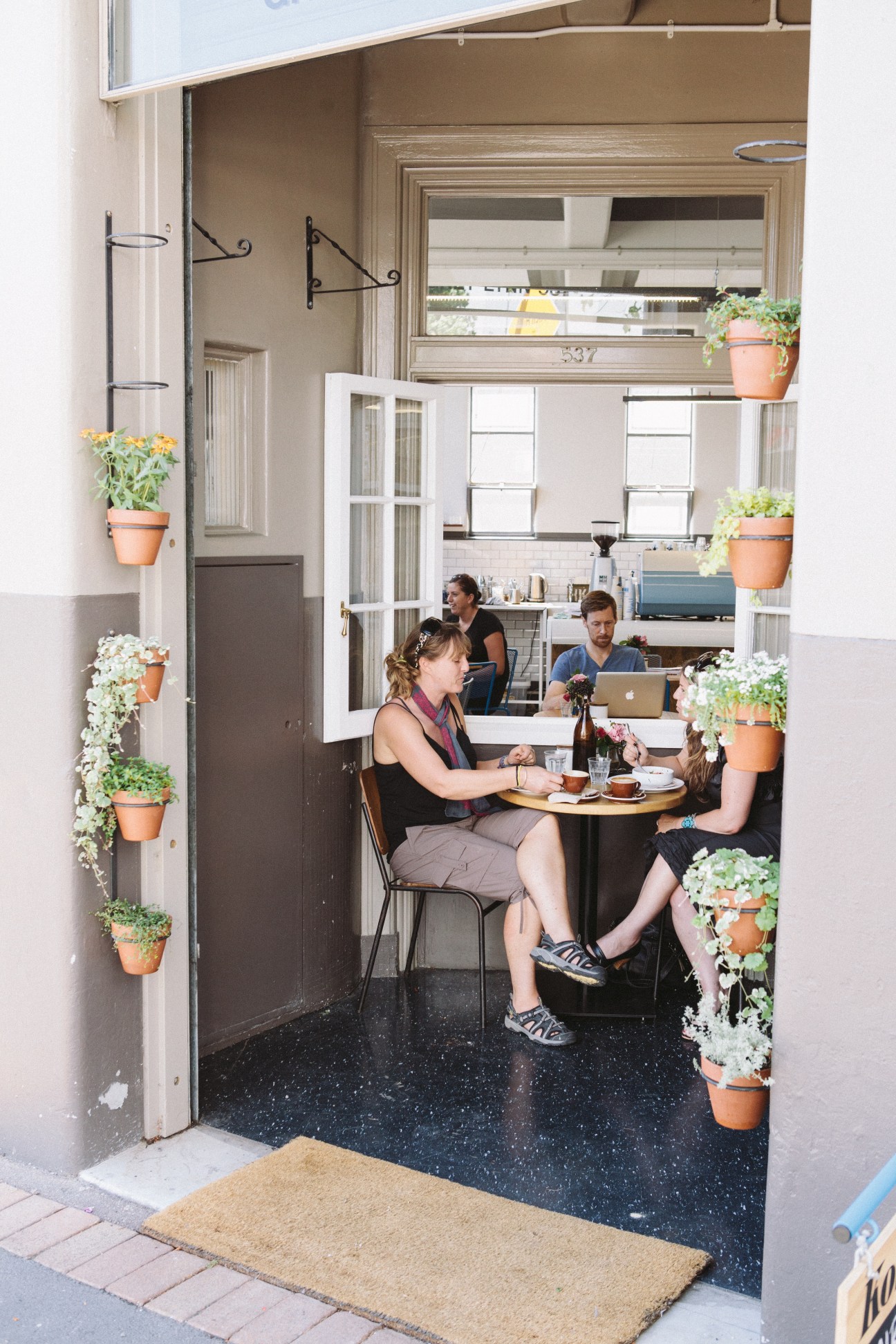 Customers dining at Kokako café in a converted post office with hanging potted plants flanking the entrance.
