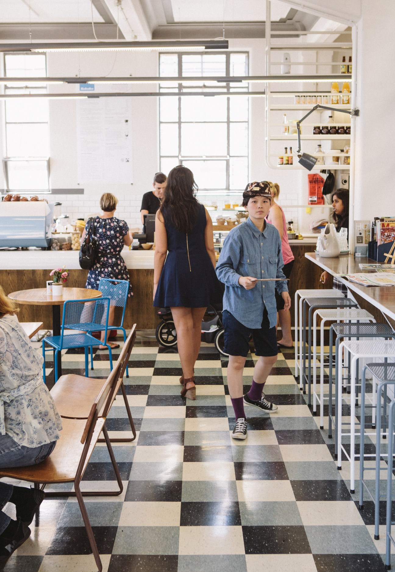 Interior of Kokako café in Auckland showing customers at tables and counter with checkered floor and large windows.