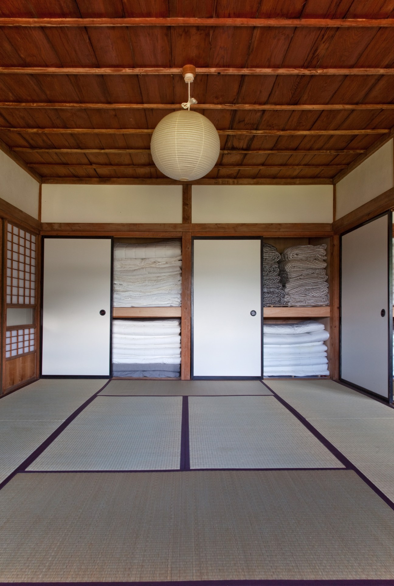 Traditional Japanese tatami room with futon mattresses stored in wall alcoves and paper lantern light fixture.