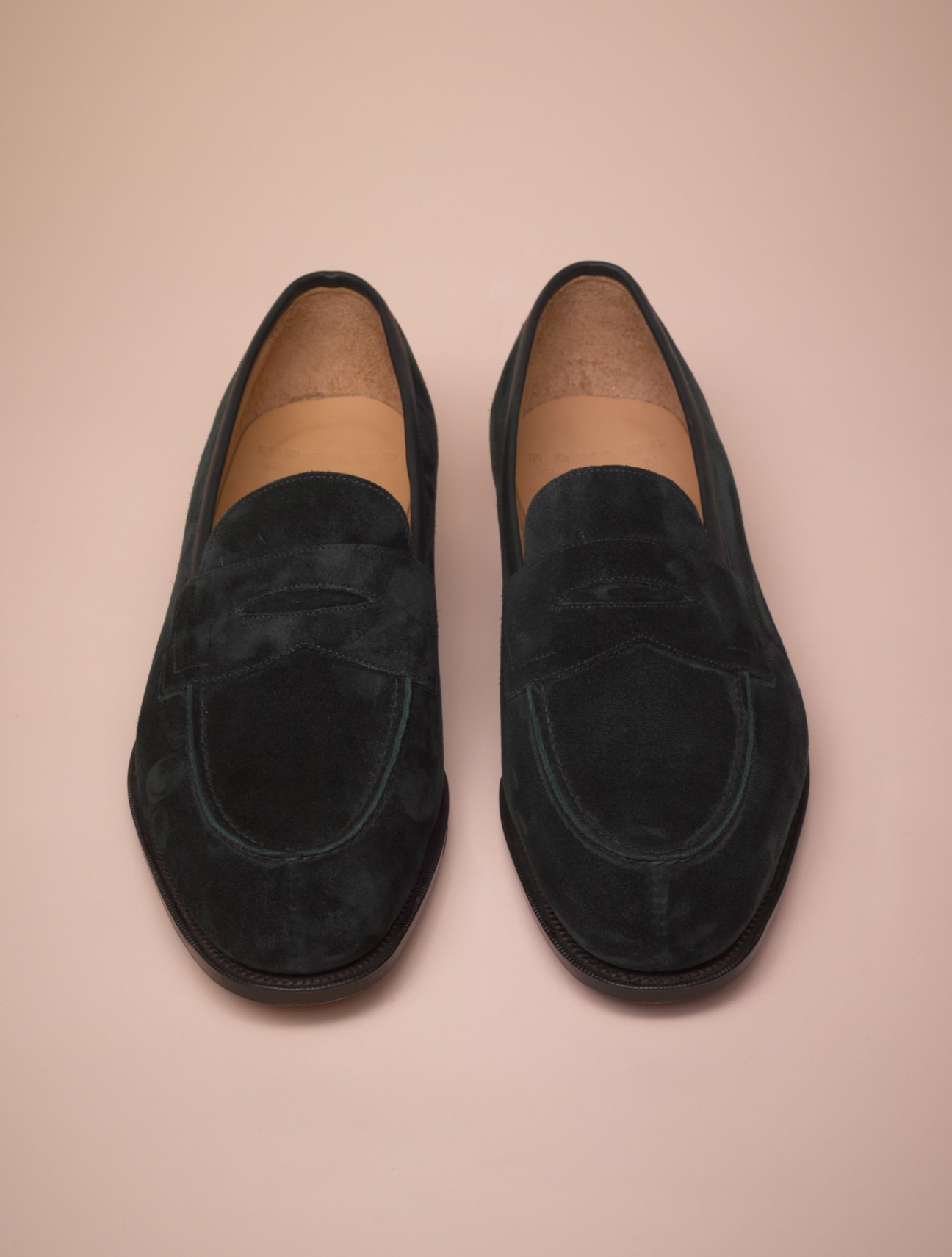 Pair of black suede loafers with tan leather trim on a beige background.