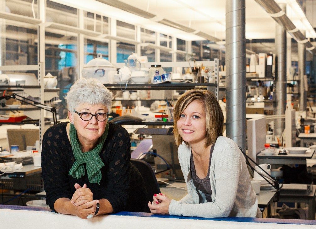Judith Sørensen and Jacqueline Tranemose Fredericia sit together in a Royal Copenhagen studio filled with porcelain and painting supplies.