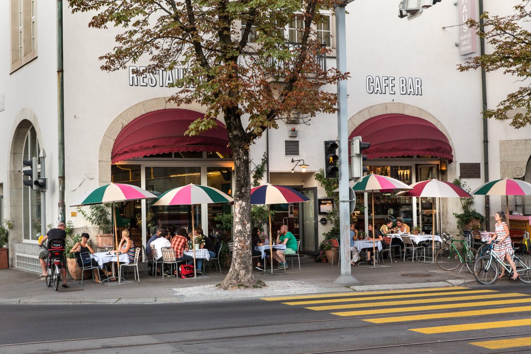 Outdoor café with colorful umbrellas and diners under red awnings at Volkshaus restaurant in Zürich.