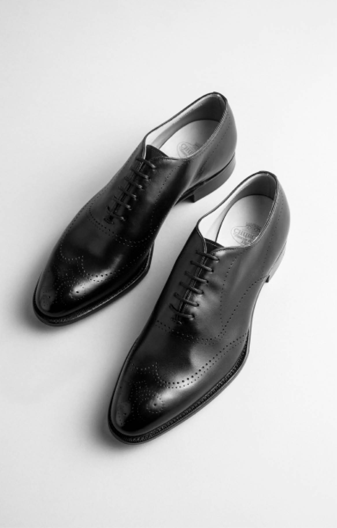 Black leather oxford dress shoes with brogue detailing photographed from above on white background