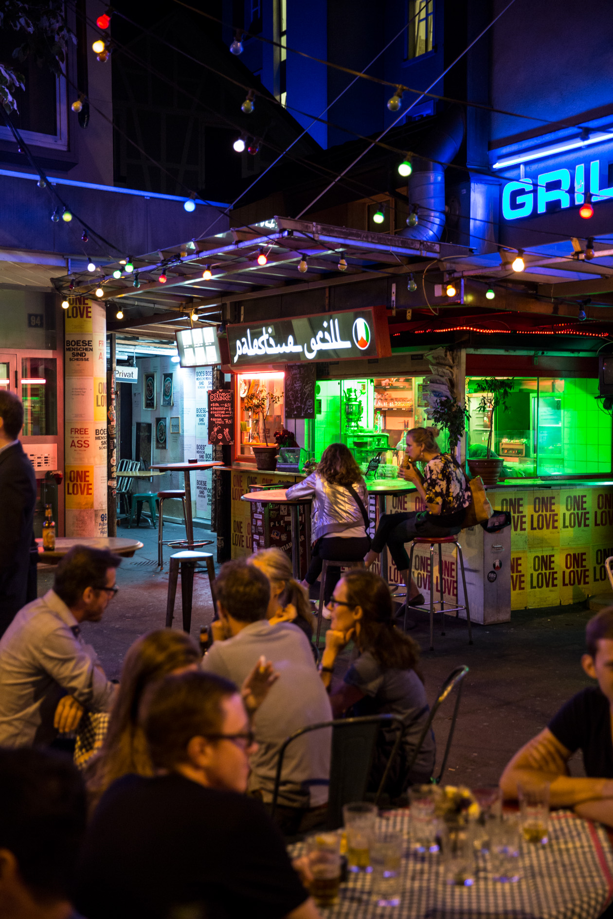 Night scene of Palestine Grill street-food stall in Zürich's Kreis 4 with neon signage and crowds of people.