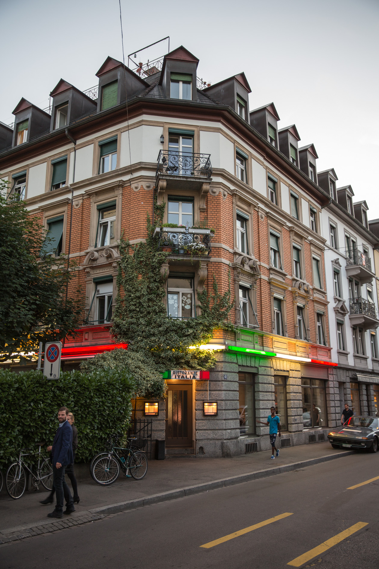 Italia restaurant building facade with ivy-covered corner, ornate stonework, and illuminated storefront signage on Zürich street.