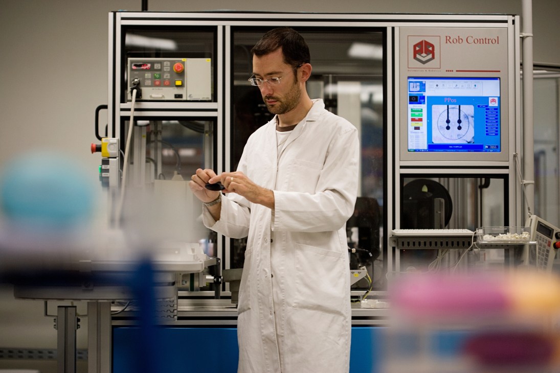 Lab technician manager Didier Galice in white coat working with spectacle frames at industrial equipment.