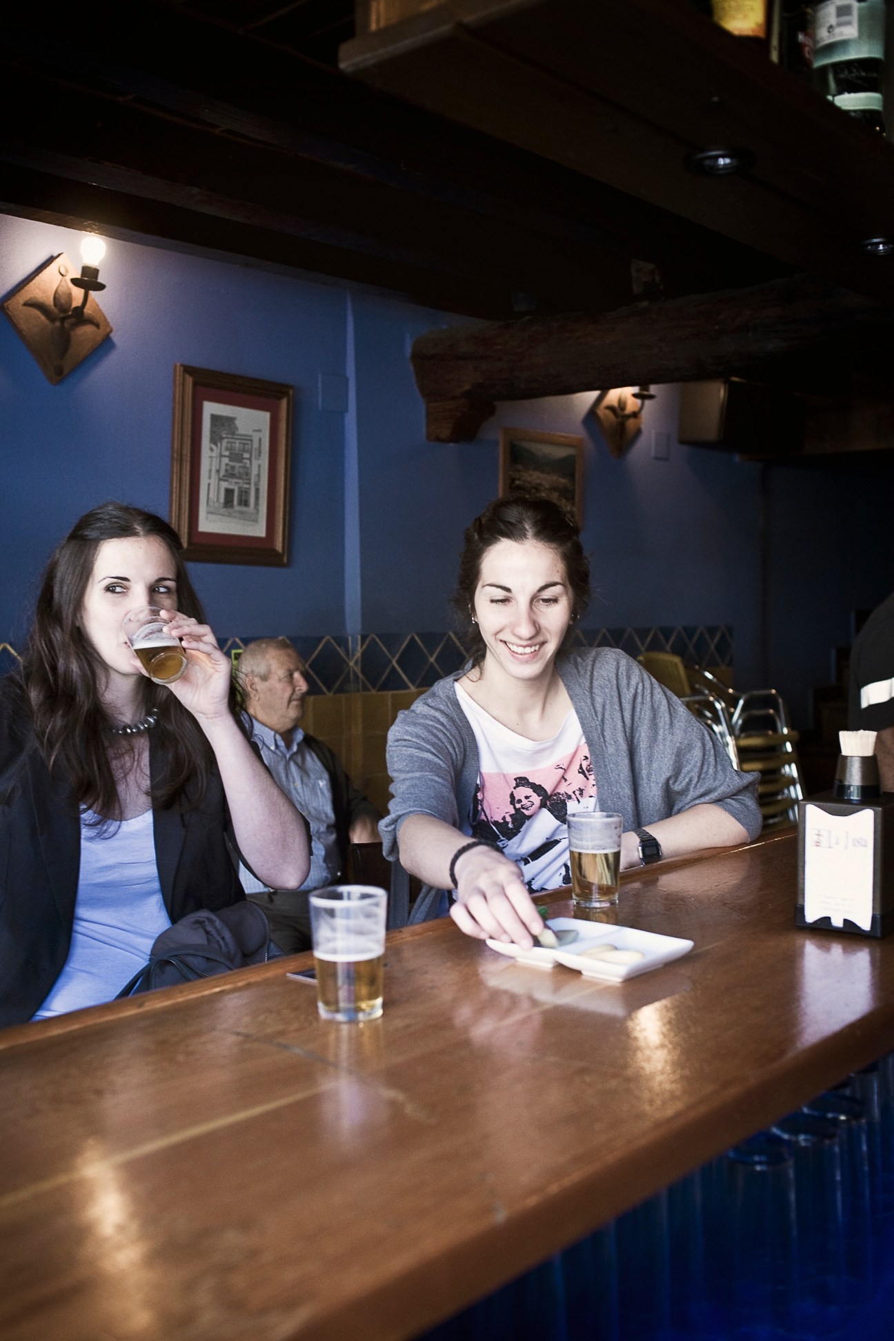 Two women enjoying drinks at a bar with blue walls and wooden beams.