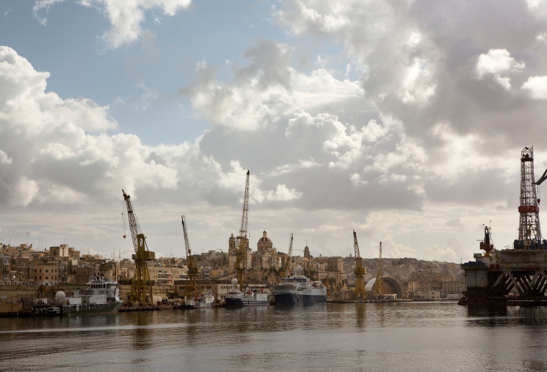 Yacht repair yard with industrial cranes and ships at Grand Harbour, Valletta waterfront with historic stone buildings.
