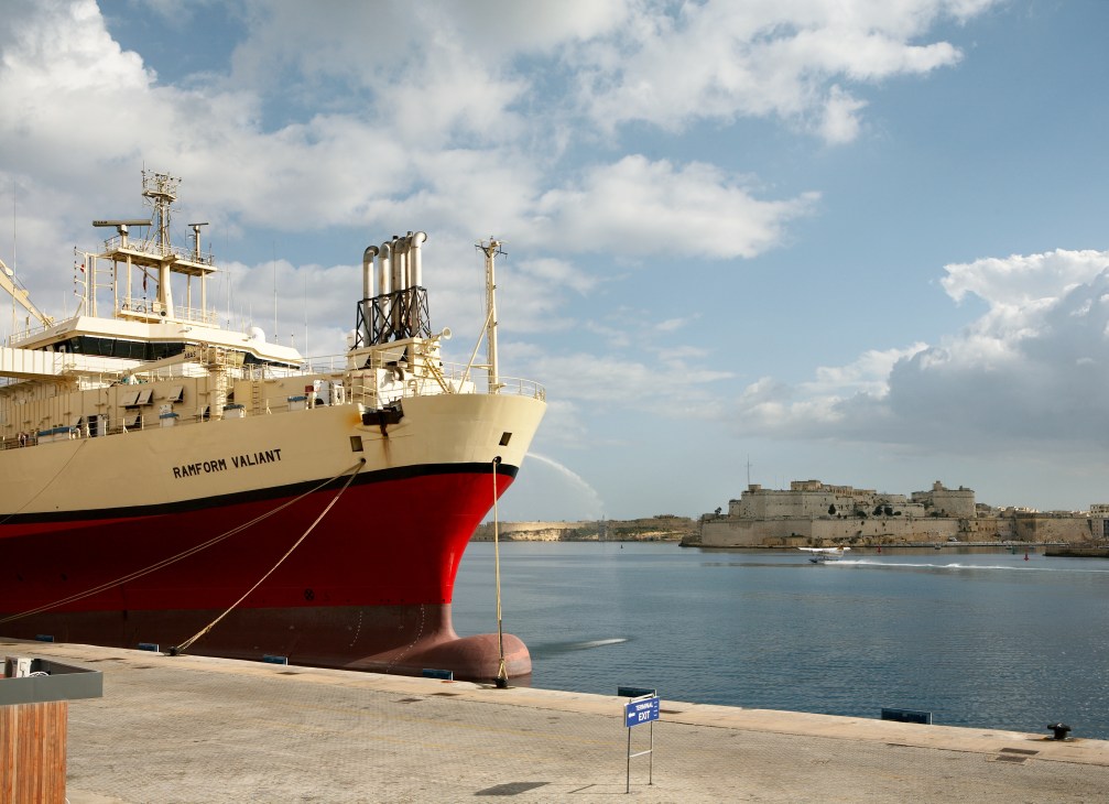 Red and cream cargo ship Rahform Valiant moored in Malta's Grand Harbour with fortifications visible across the water.