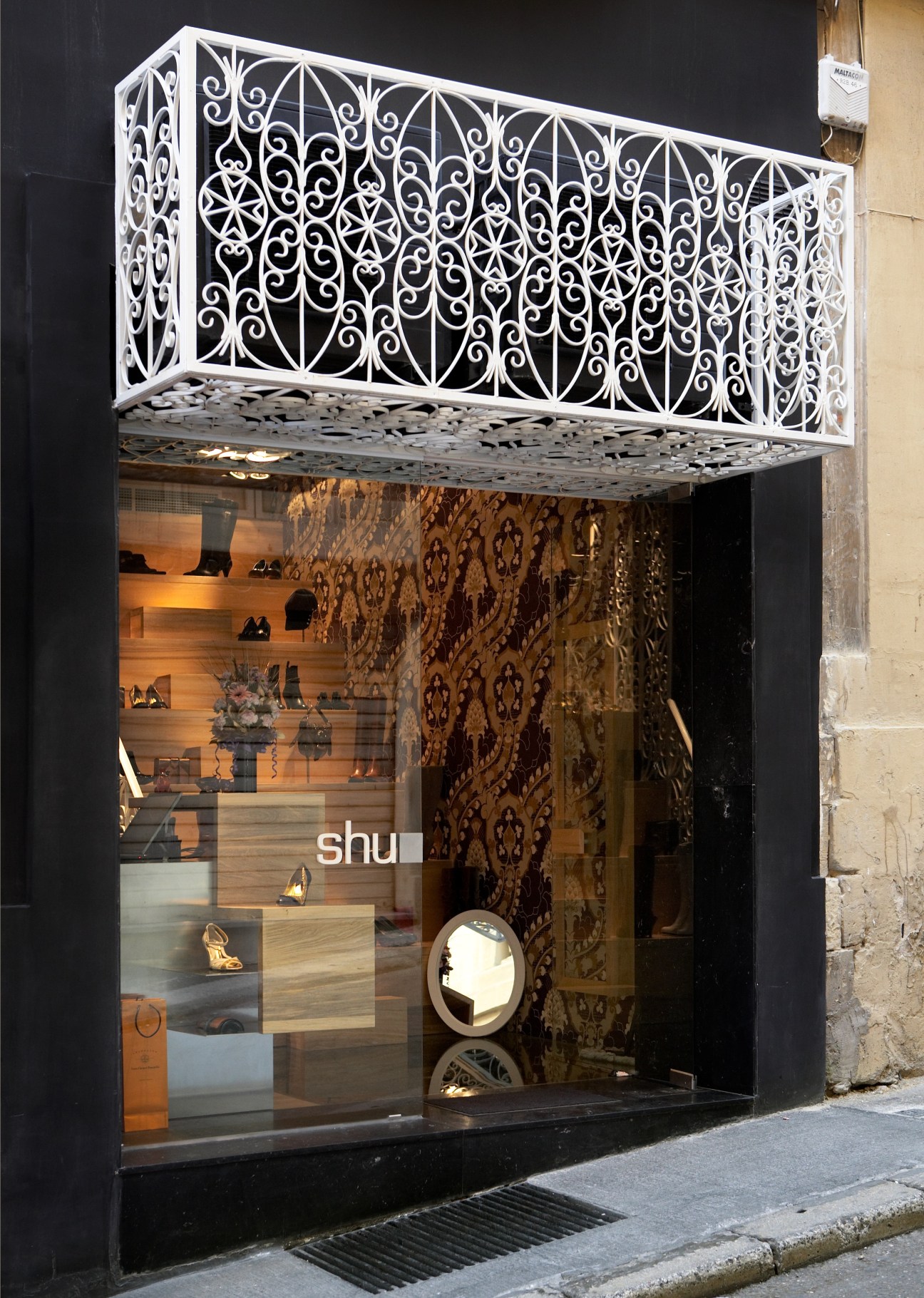 The Shu franchise storefront with ornate white metalwork awning and dark facade displaying shoes.