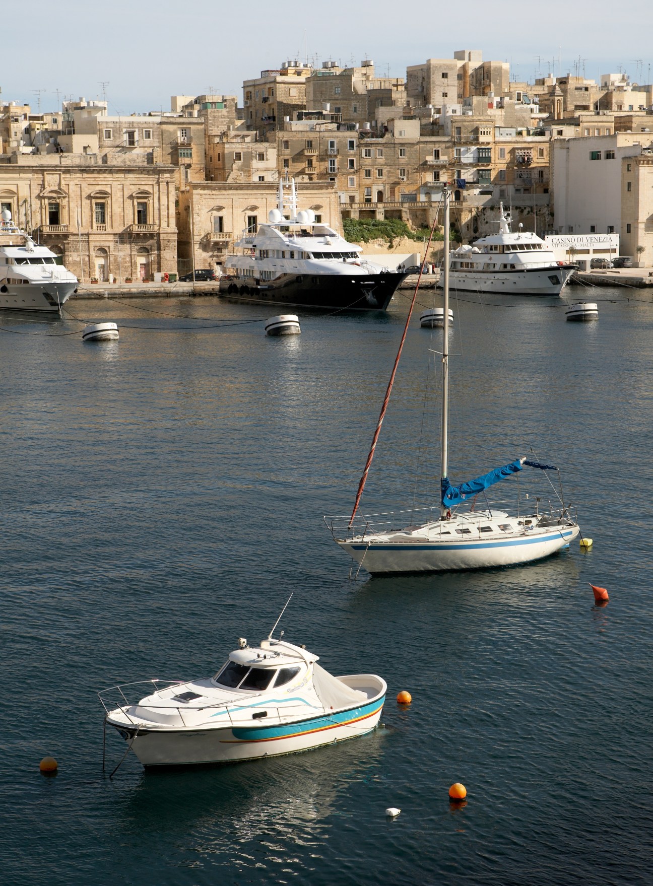 Cottonera waterfront with moored boats and historic stone buildings rising behind the harbor.