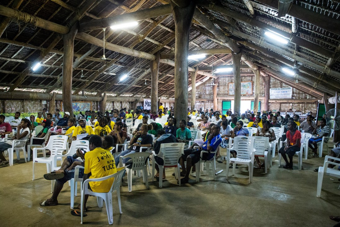 Large indoor meeting with many attendees seated in white plastic chairs at a youth justice conference in Vanuatu.