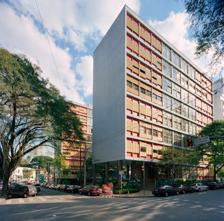 Modernist apartment building with red and yellow facade surrounded by trees in São Paulo.