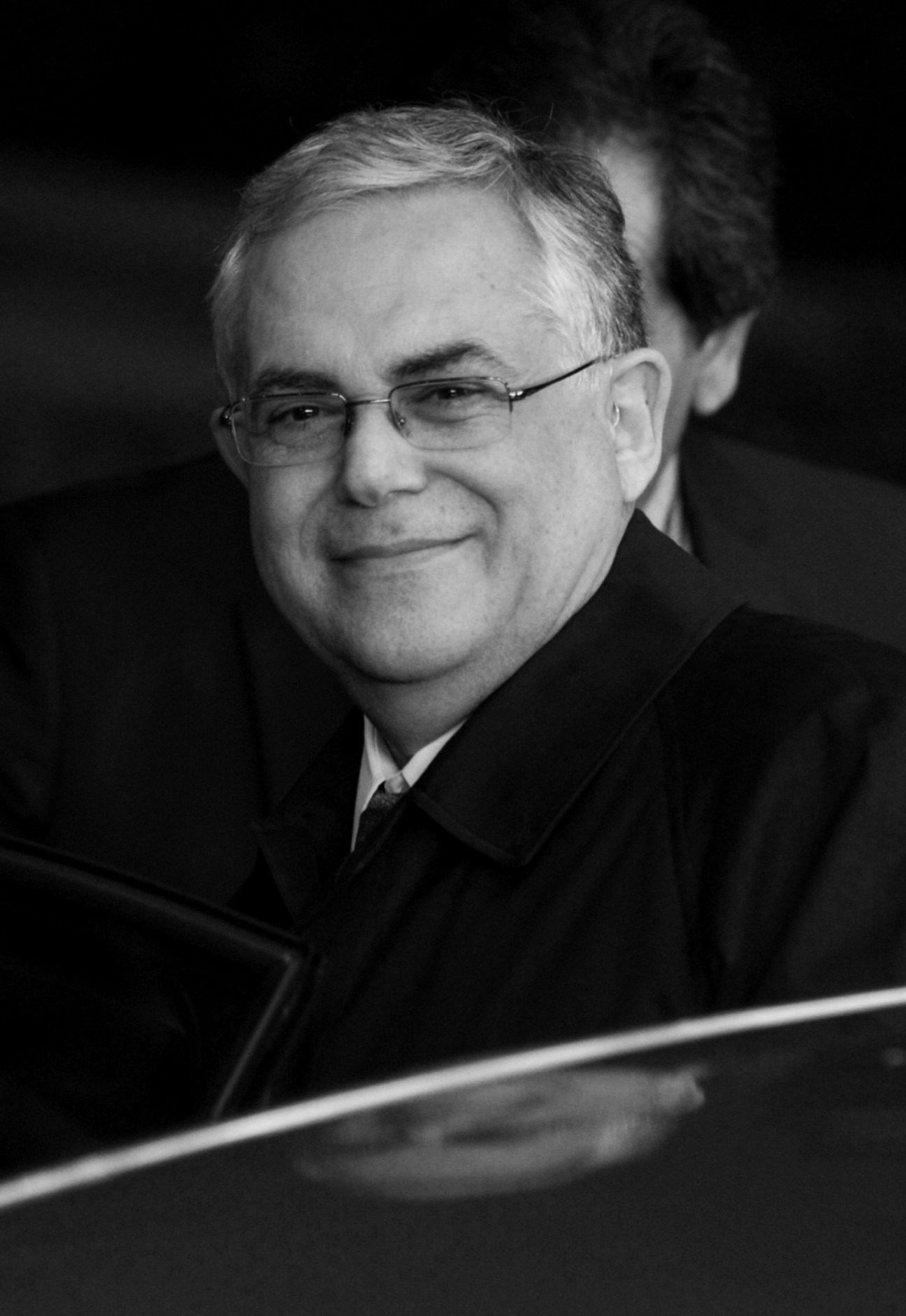 Black and white portrait of Lucas Papademos, Greek prime minister, wearing glasses and formal suit in a car.