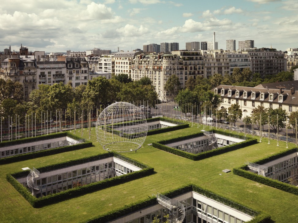 Aerial view of Unesco's Paris headquarters forecourt with Erik Reitzel's Symbolic Globe sculpture surrounded by green lawns and flags.