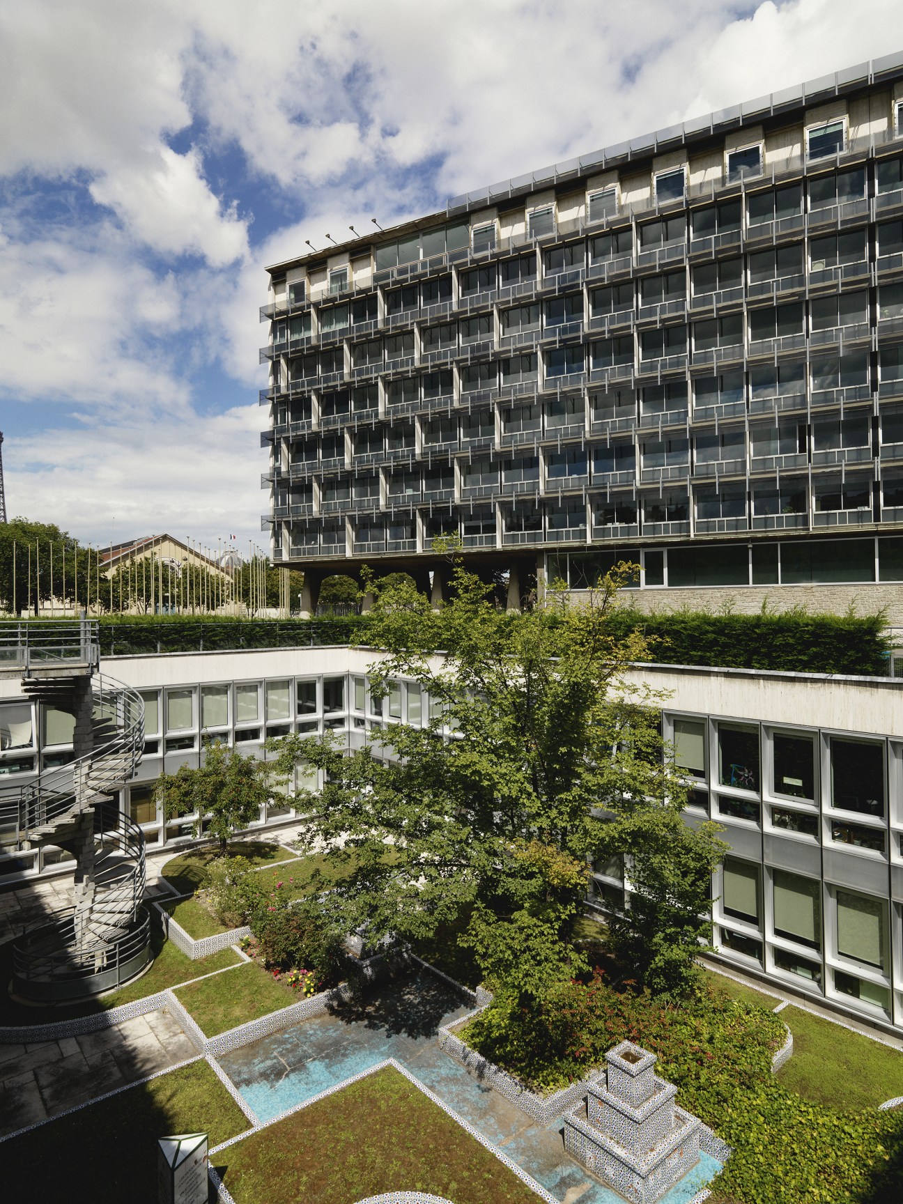 Modernist Unesco headquarters with curved garden featuring greenery, trees and water features below.