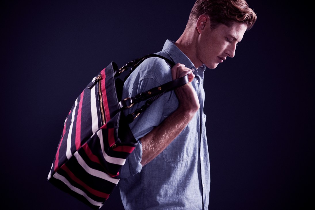 Man wearing light blue shirt with red, white and navy striped Frank Daniel bag over shoulder.