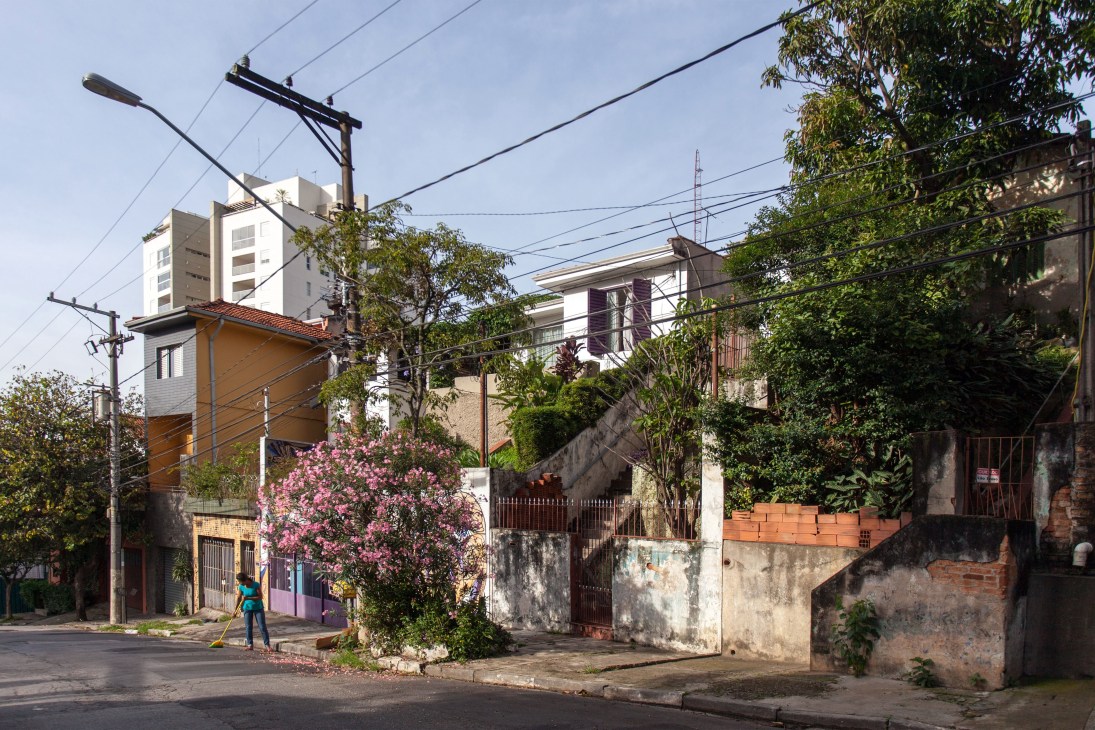 Vila Madalena street with low-rise buildings, pink flowering tree, and power lines under blue sky.