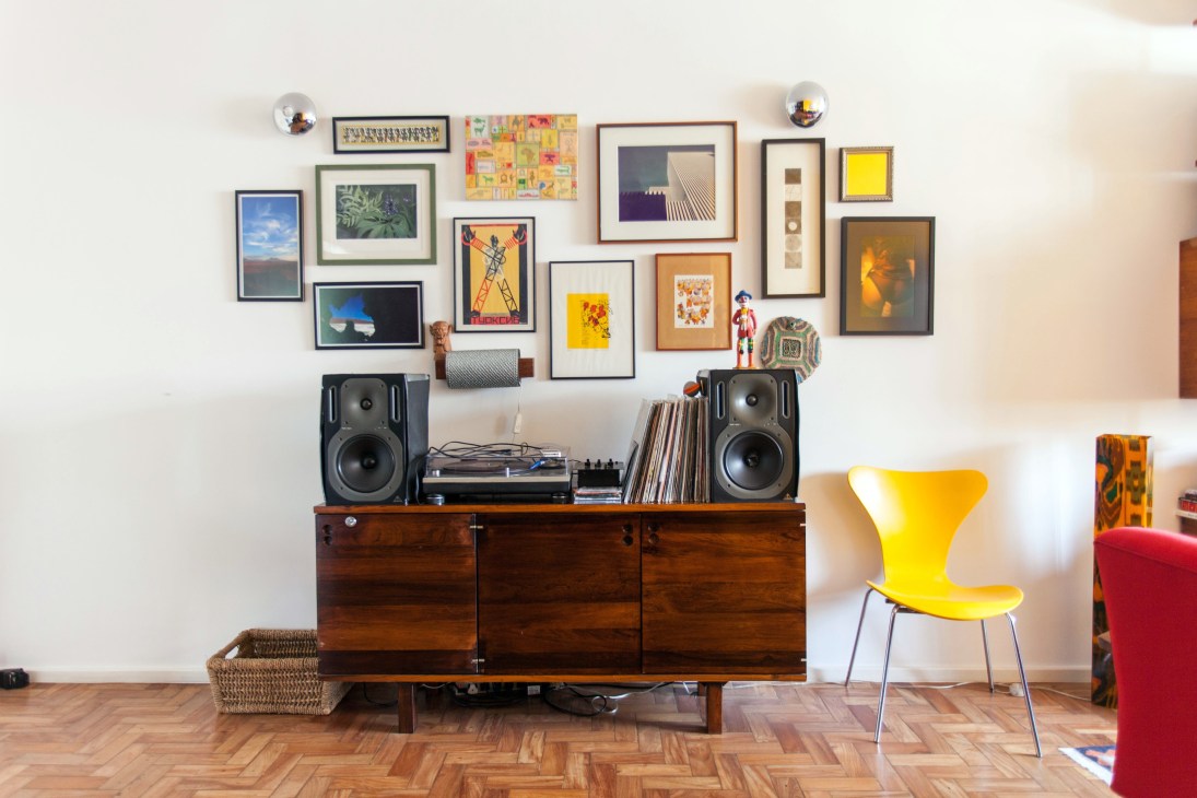 Interior of Rica Amabis and Bel Coelho's home with a wooden credenza, speakers, vinyl records, and a gallery wall of framed artwork above.