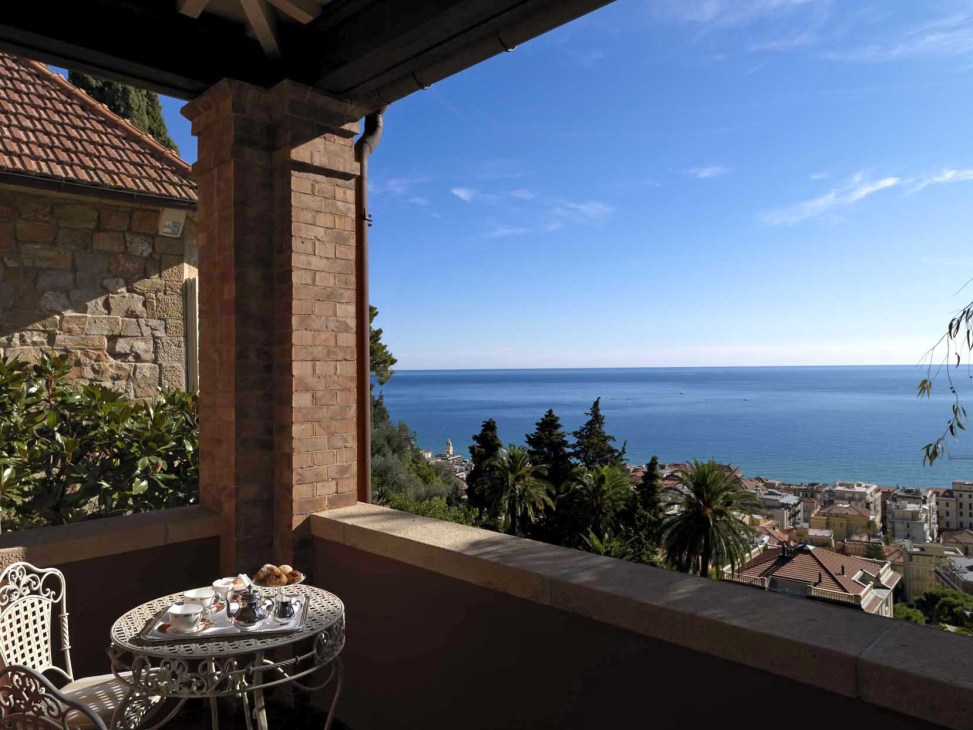 A seaside terrace with wrought iron furniture overlooking the Gulf of Alassio and Mediterranean Sea.