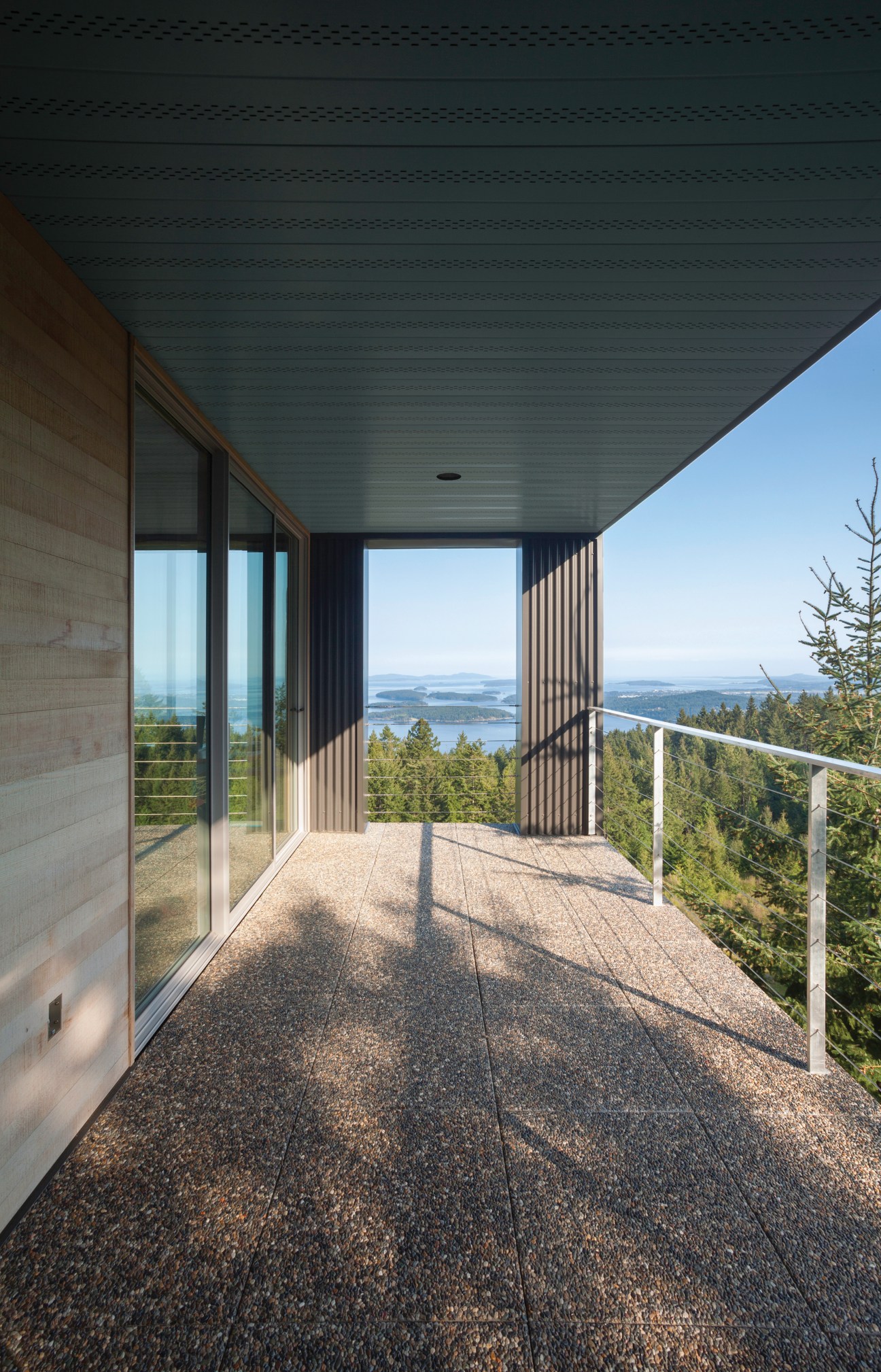 Modern wooden balcony overlooking forested landscape and water with metal railings and geometric ceiling