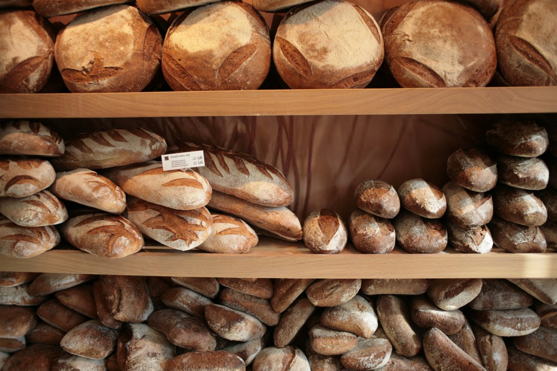 Shelves displaying various types of fresh baked bread loaves and round artisan breads at Vlaamsch Broodhuys.