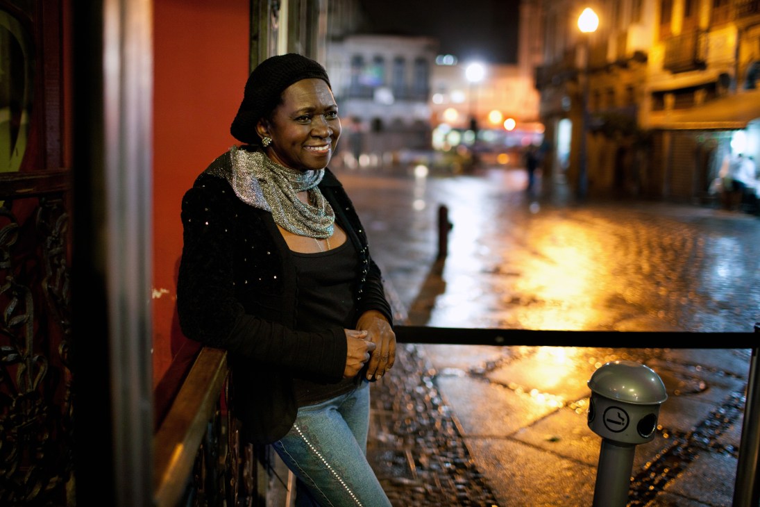 Áurea Martins smiling on a nighttime street in Rio de Janeiro's Lapa district.