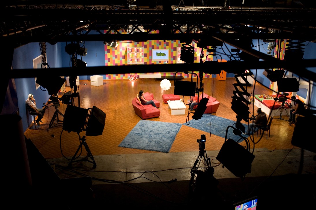 Television studio set with colorful backdrop, red furniture, and professional lighting equipment overhead.