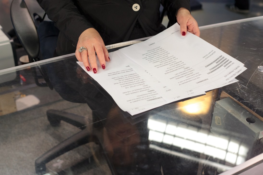 Woman's hands with red nails holding news scripts on a desk, showing broadcast notes.