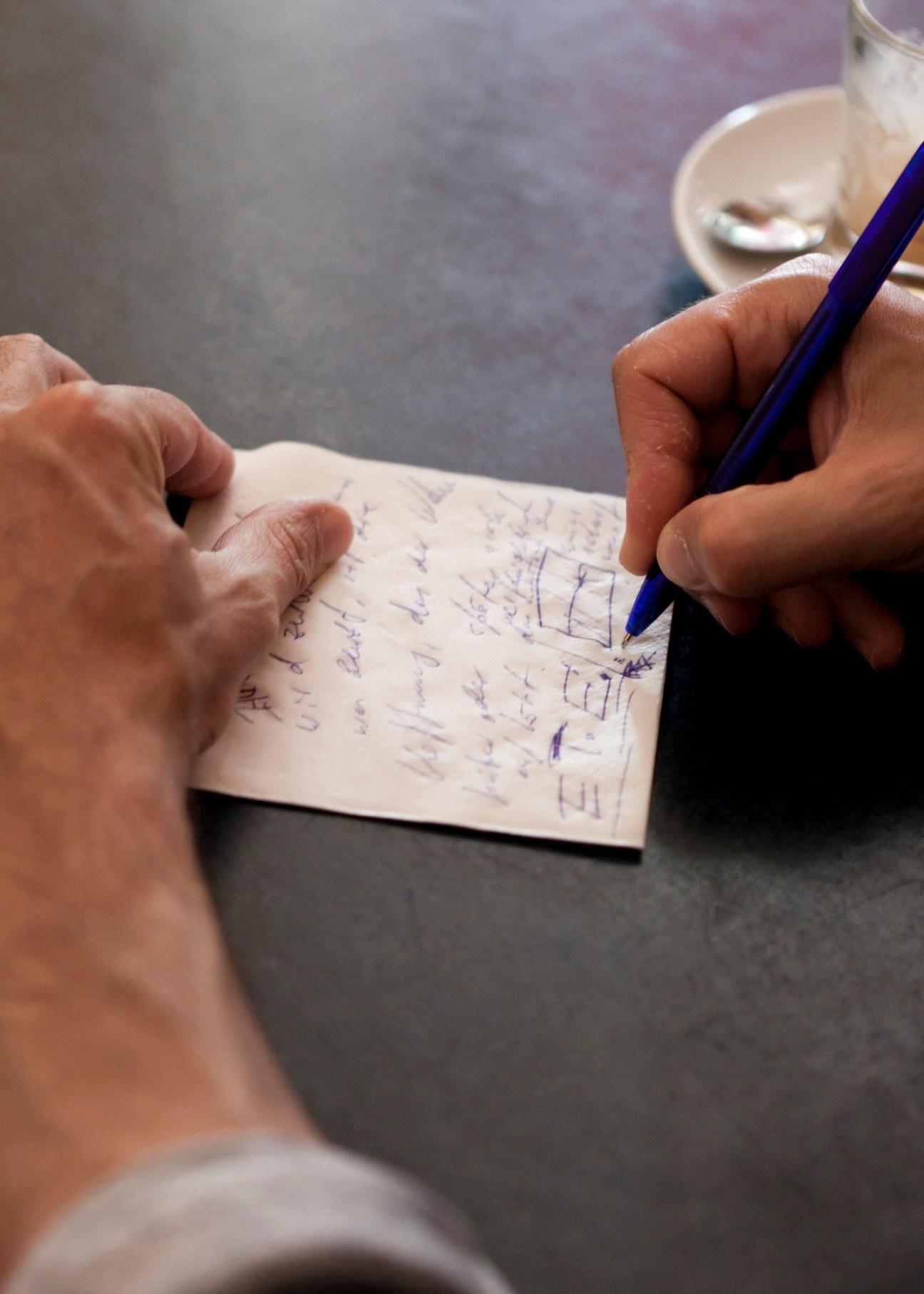 Hands holding a blue pen writing notes on a white notepad.
