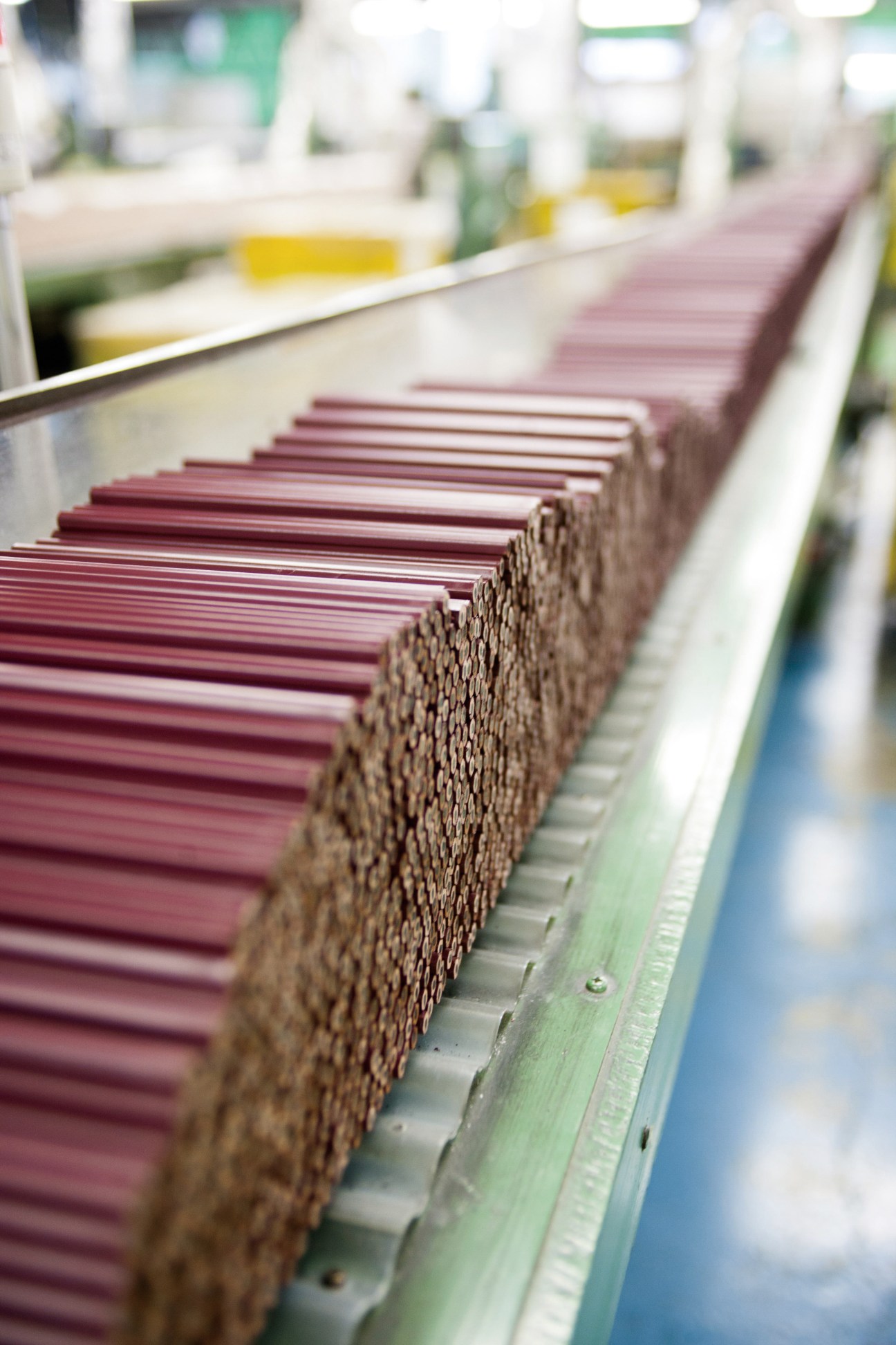 Stacked burgundy vintage-style pencils lined up on a conveyor belt in a factory setting.