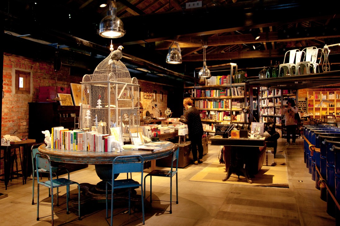 Interior of VVG Thinking bookshop with bookshelves, pendant lights, and shoppers browsing merchandise.