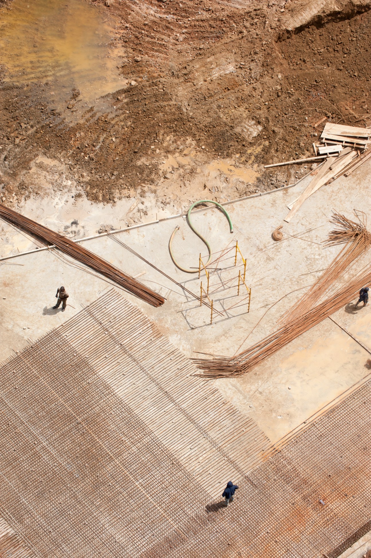 Aerial view of construction site with workers, metal framework, and building materials on concrete foundation.