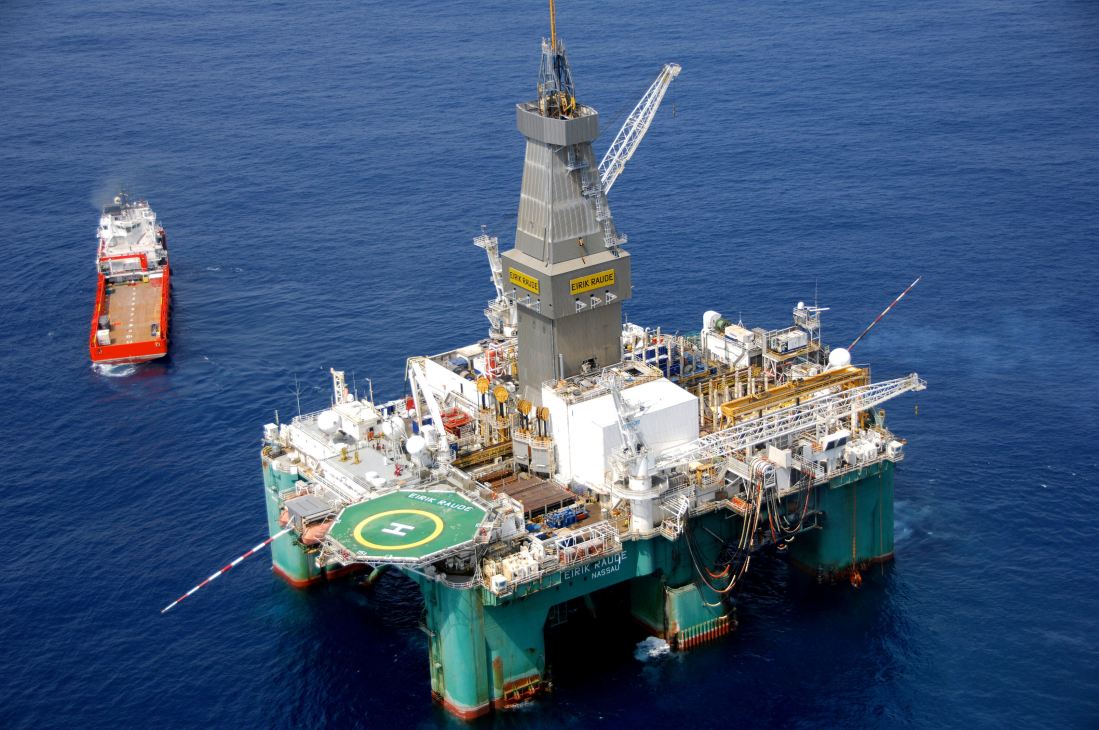 Offshore oil drilling platform with support vessel in blue ocean waters.