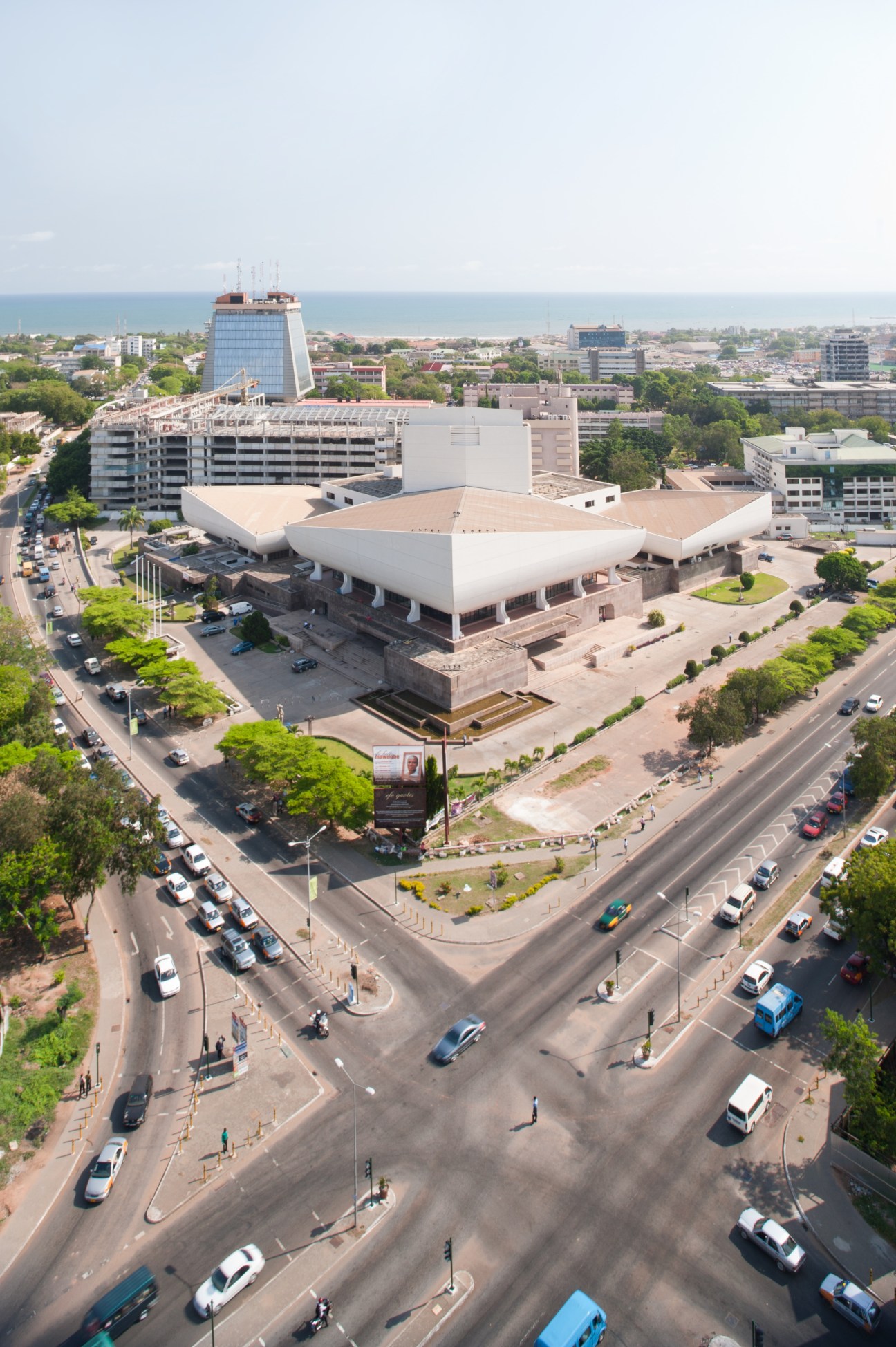 Aerial view of Ghana's National Theatre, a modern white building with curved architecture surrounded by streets and urban development near the coast.