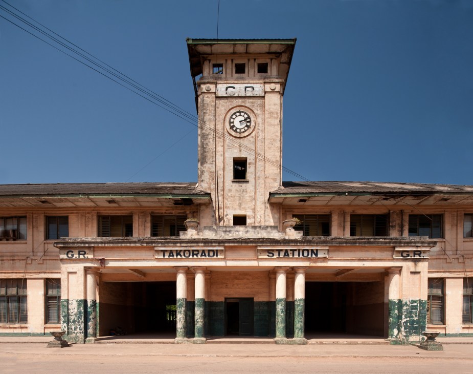 Abandoned Takoradi Train Station with clock tower and peeling pink facade.