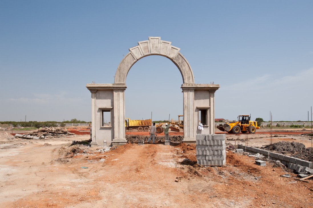 Ornamental arch entrance under construction at Trasacco Valley luxury development with heavy machinery and red soil