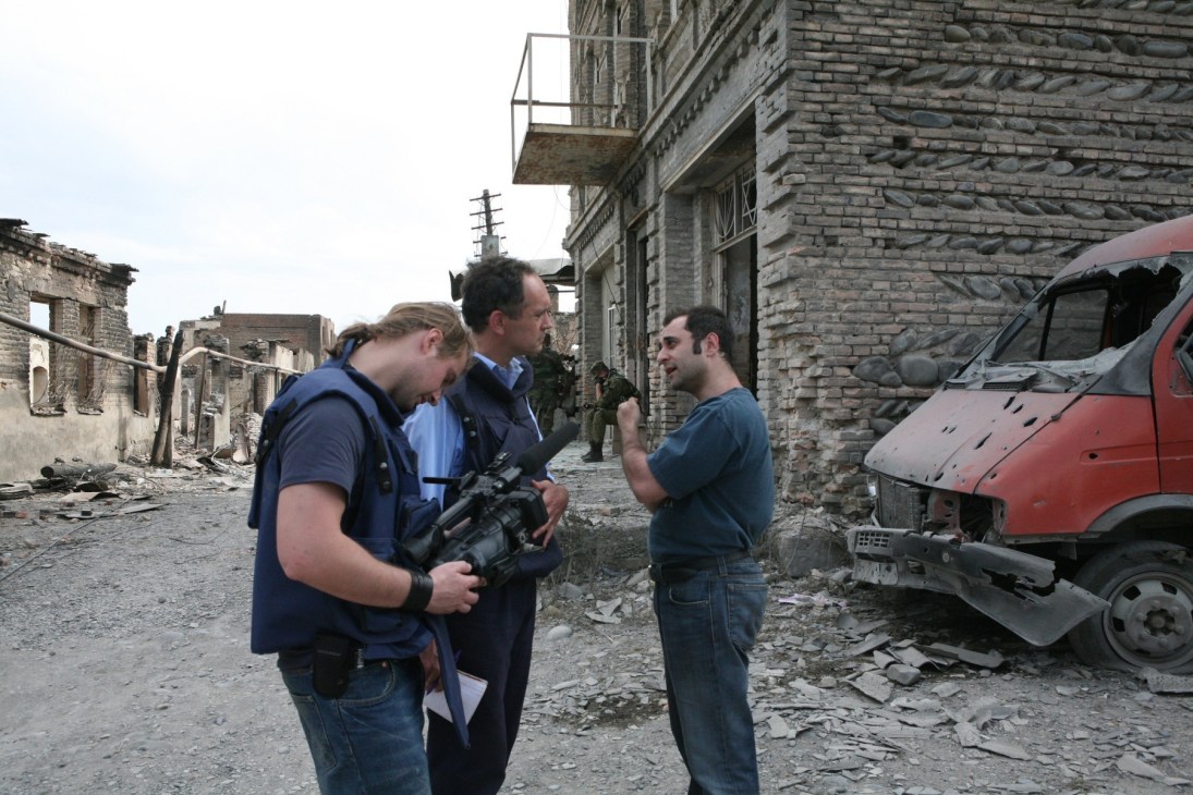A Russian government official speaks with an ITN film crew holding a camera in a destroyed street in Tskhinvali.