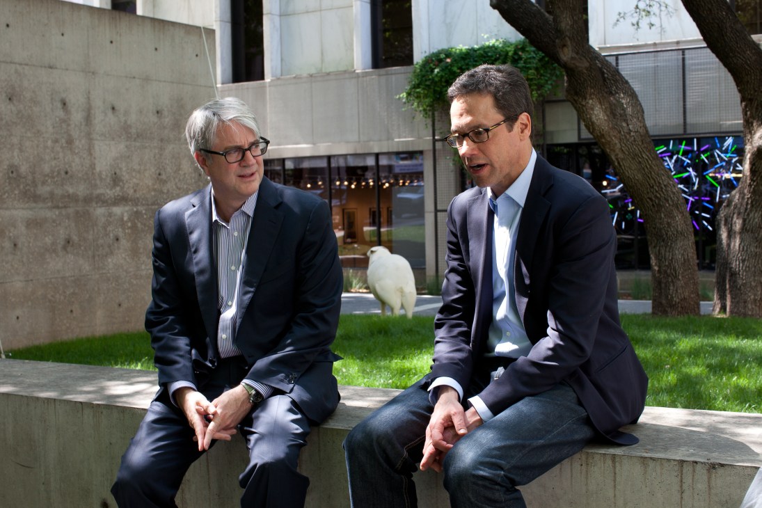 Dallas Art Fair founders John Sughrue and Chris Byrne seated outdoors in conversation.