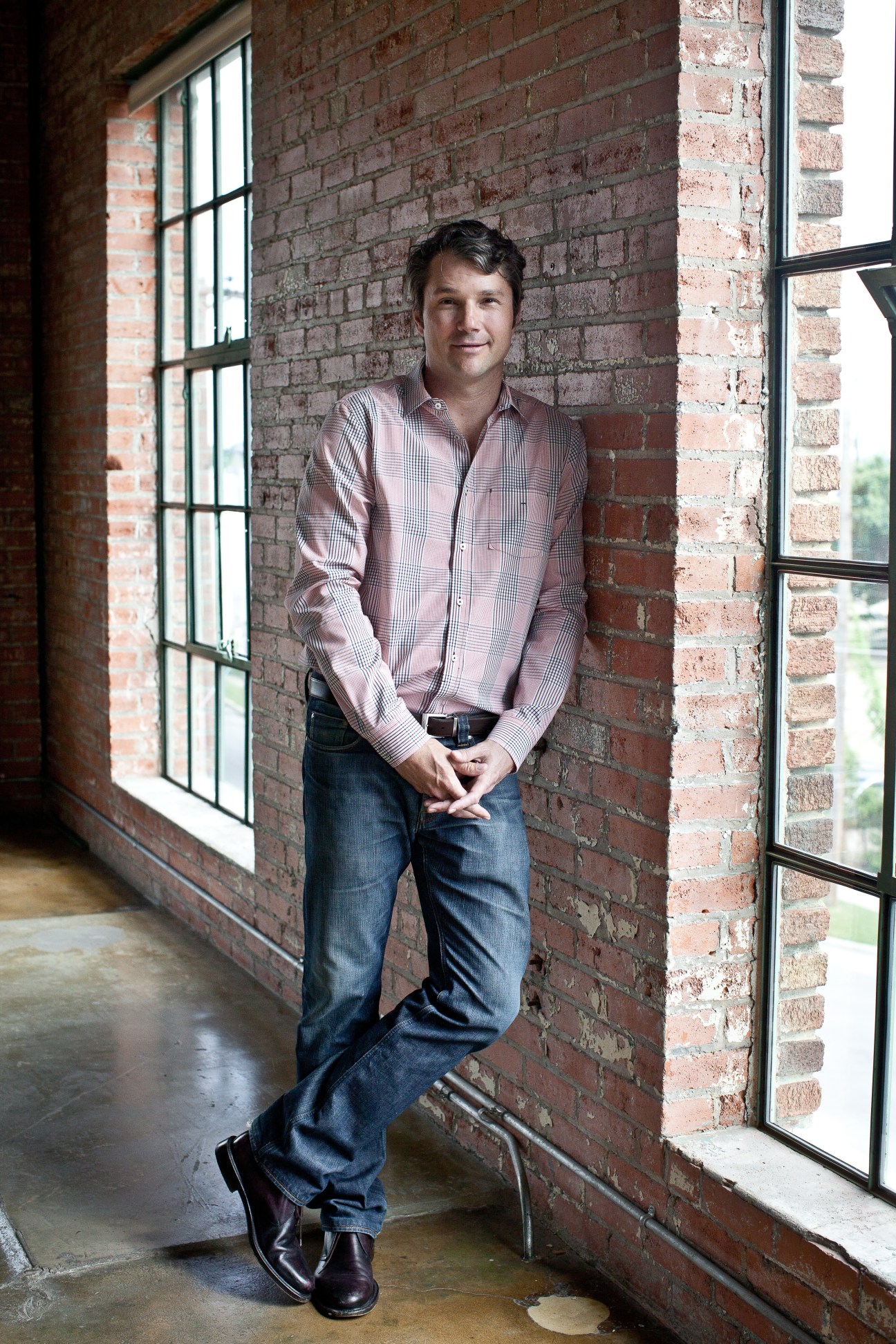 Collector Alden Pinnell stands against a red brick wall between two industrial windows in an industrial loft space.