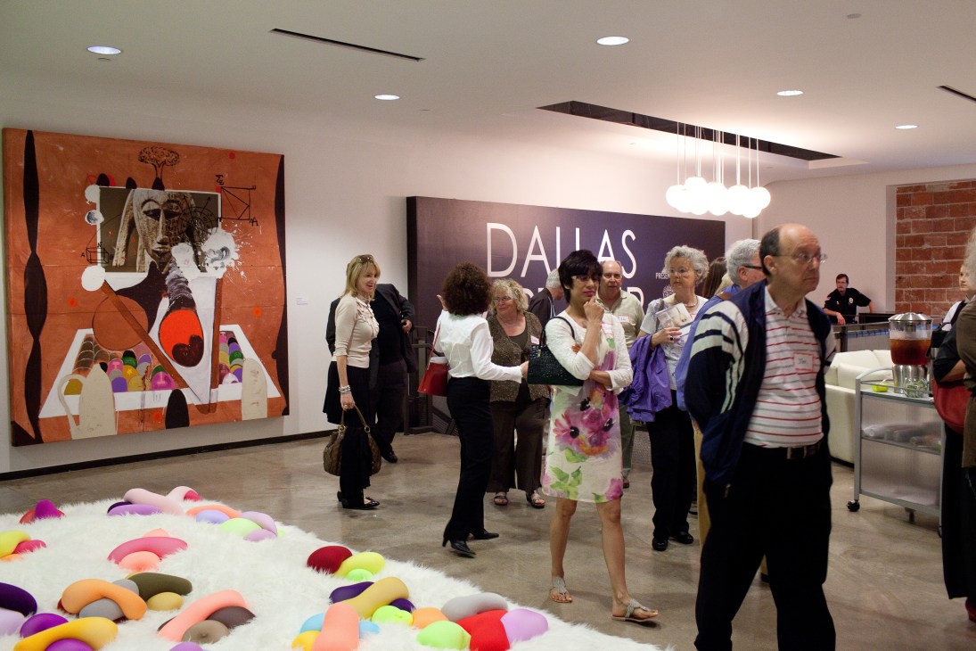 Visitors browse artworks at the Dallas Art Fair, with colorful abstract sculptures in foreground and orange artwork on wall.